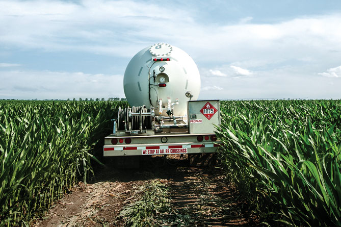 A propane truck driving down a dirt road through a corn field