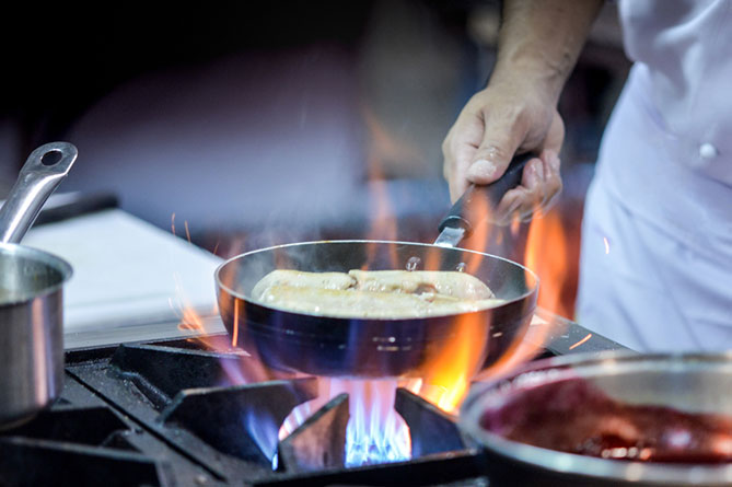 A person cooking over an open flame on a stove inside a commercial kitchen